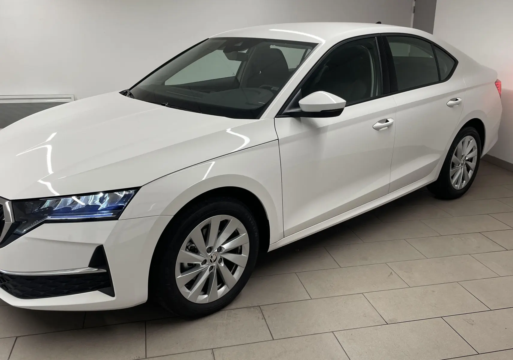 Skoda Octavia 2024 blanc candy vue 3/4 avant droit, phares allumés et jantes alliage, intérieur sombre visible.