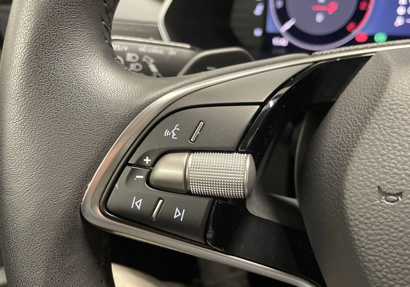 Gros plan sur les commandes gauche du volant noir d'une Skoda Octavia 2024, avec molette crantée et boutons multifonctions.