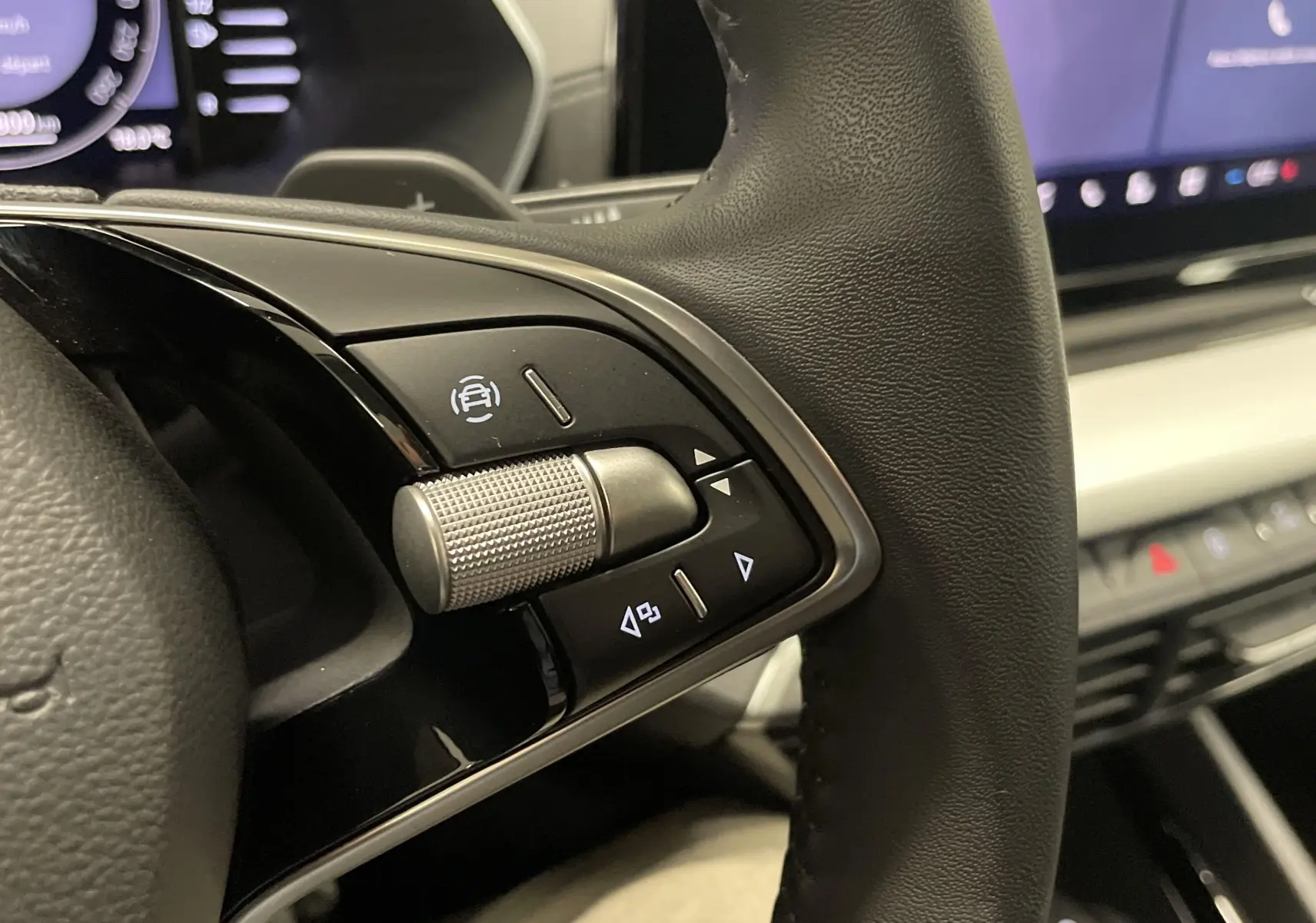 Gros plan sur les commandes gauche du volant noir d'une Skoda Octavia 2024, tableau de bord et écran tactile en arrière-plan.