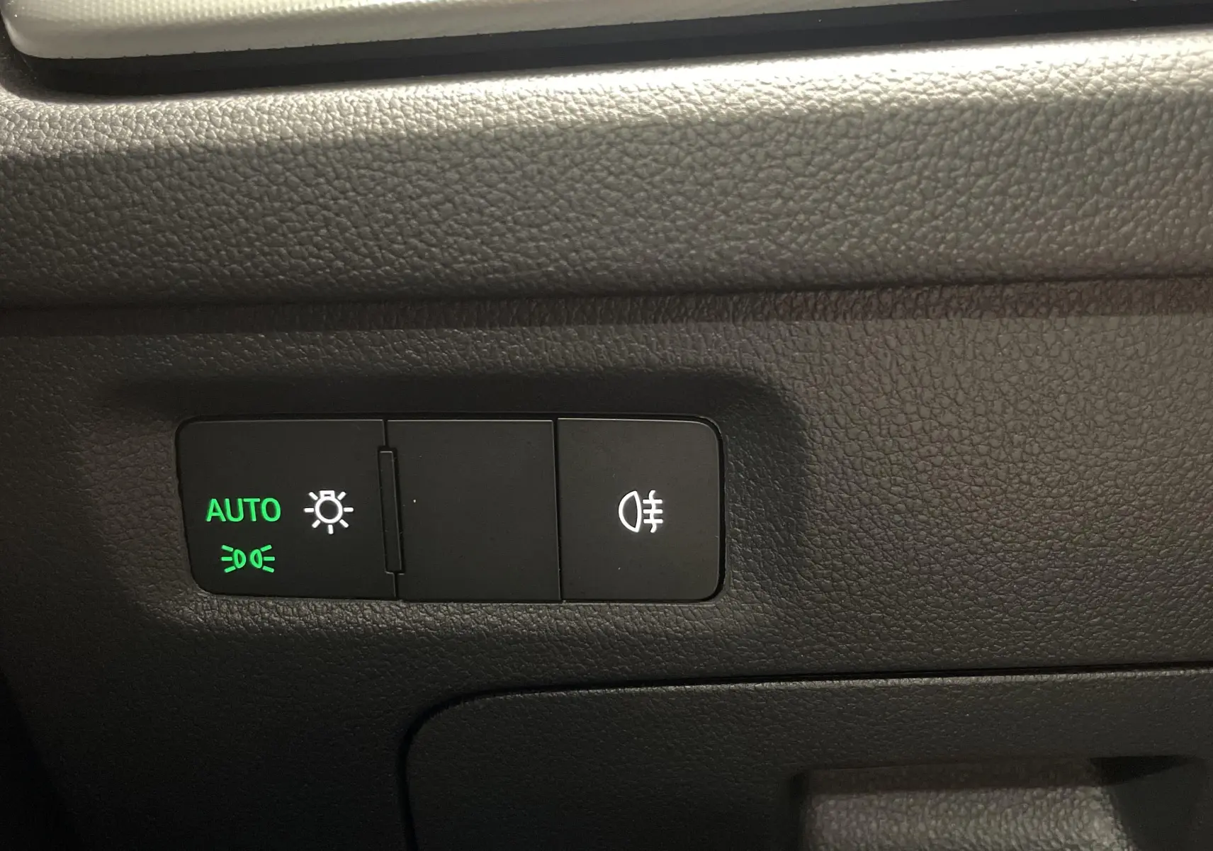 Boutons de commande des feux avec mode automatique activé, sur la planche de bord noire d'une Skoda Octavia 2024.