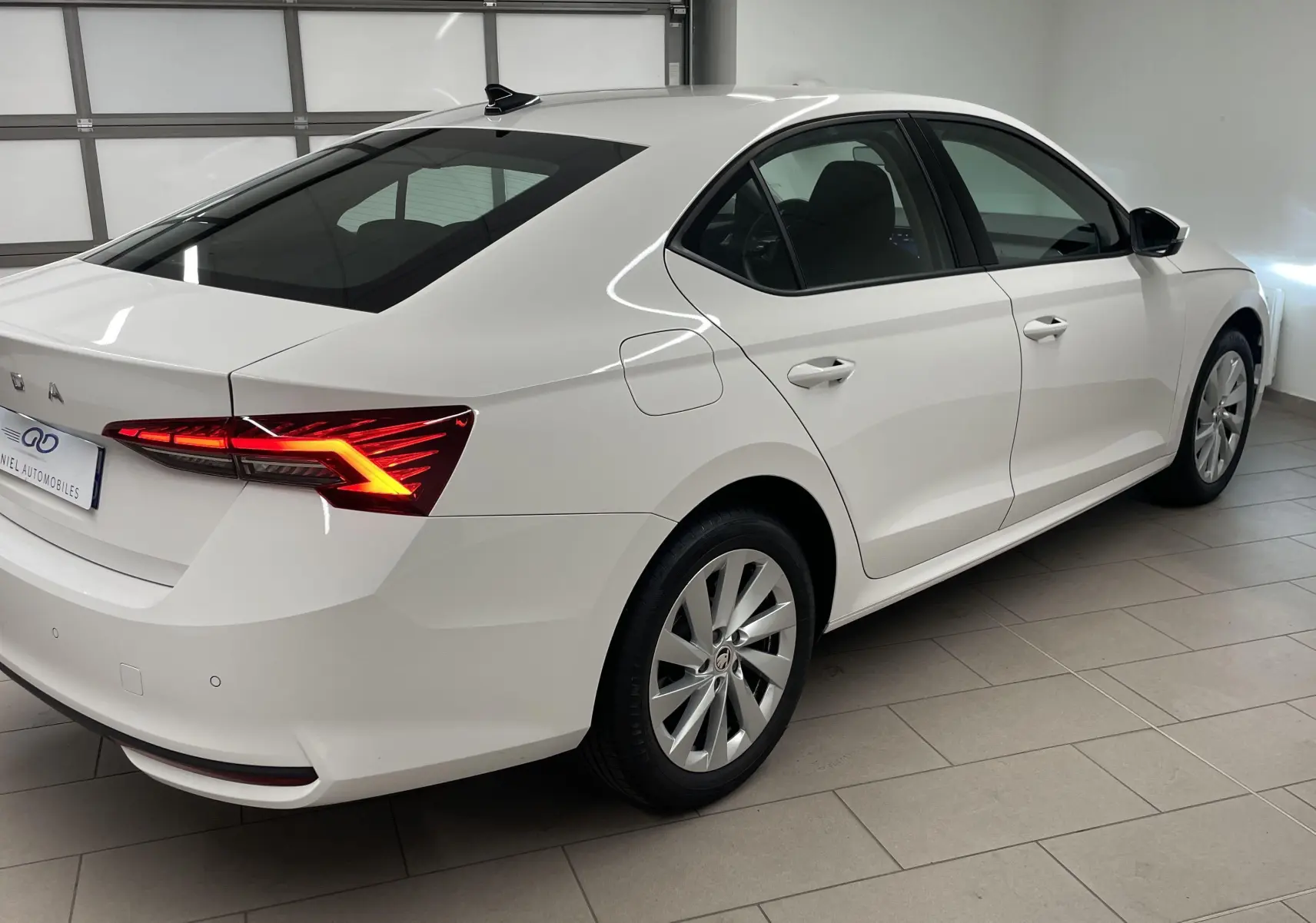 Vue 3/4 arrière droite d'une Skoda Octavia 2024 blanche Candy avec feux arrière allumés dans un garage.