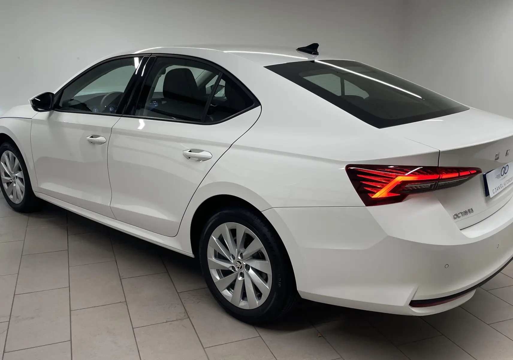 Vue 3/4 arrière droite d'une Skoda Octavia 2024 blanc candy avec feux arrière allumés en intérieur showroom.