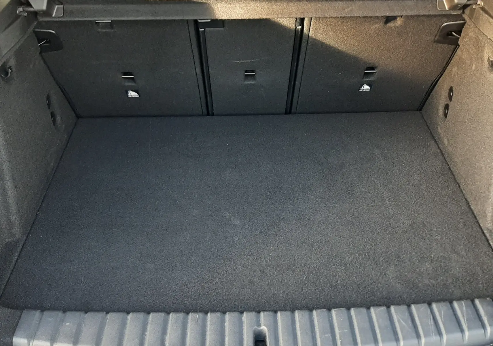 Coffre ouvert vu de l'arrière d'une BMW Série 1 gris Skyscraper, montrant l'espace de chargement vide et la banquette rabattable.