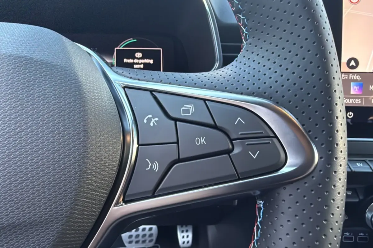 Gros plan sur les commandes au volant perforé de la Renault Clio V E-Tech 145 Esprit Alpine 2025, intérieur noir.