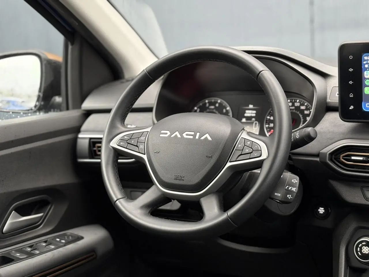 Vue intérieure centrée sur le volant noir du Dacia Sandero Stepway avec tableau de bord et écran tactile visible.