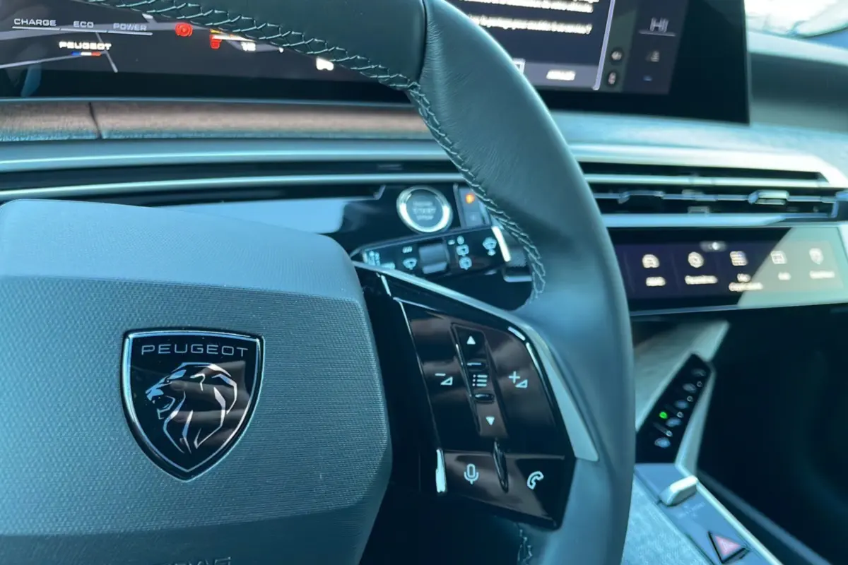 Gros plan sur le volant cuir multifonctions Peugeot 5008 Hybrid 2025 avec tableau de bord numérique et commandes tactiles.