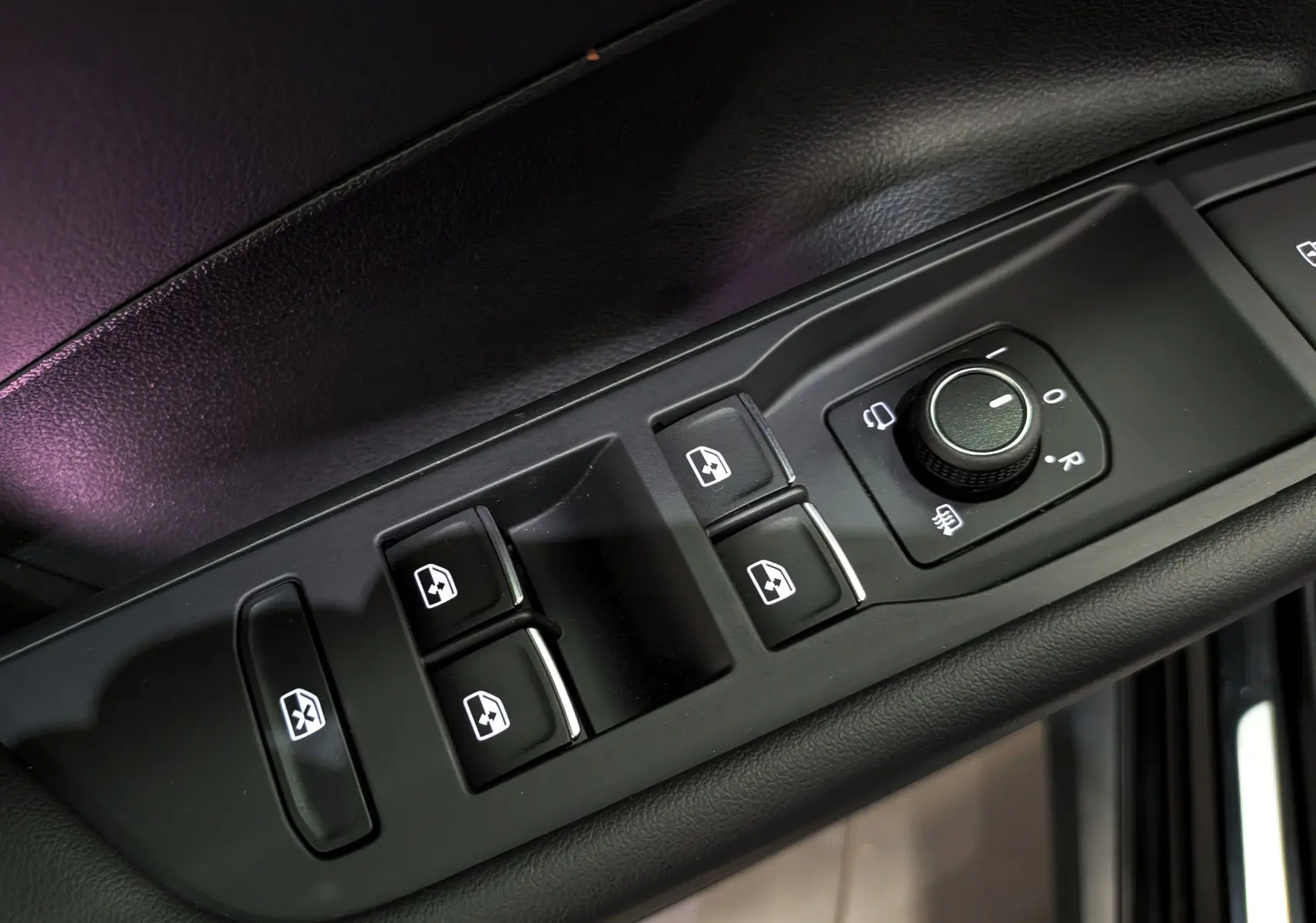 Gros plan sur les commandes de lève-vitres et réglage des rétroviseurs côté conducteur du Volkswagen T-Roc eTSI noir.