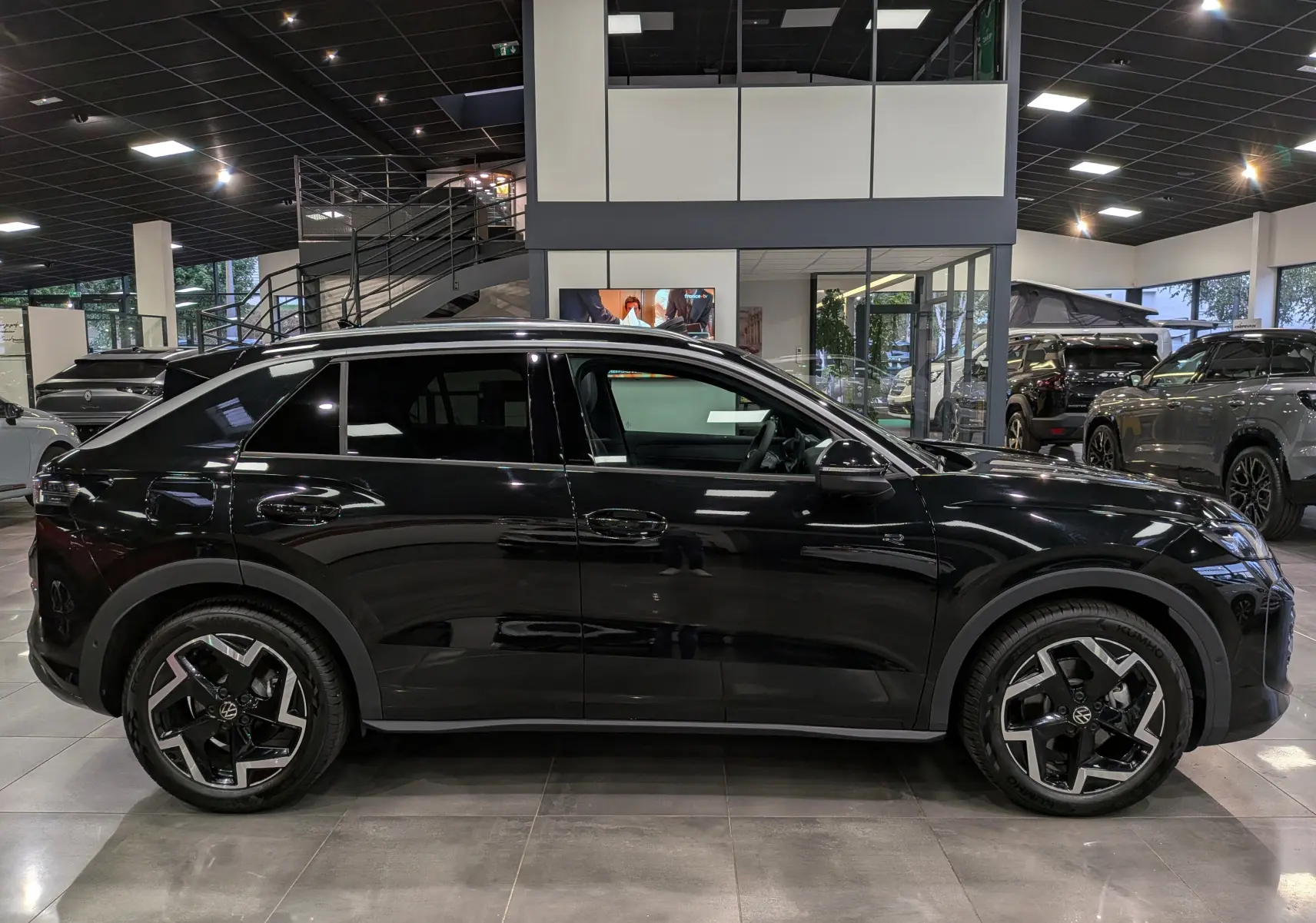 Profil côté gauche d'un Volkswagen T-Roc eTSI 150 CH DSG7 R-Line noir Ébène, avec jantes bi-ton et vitres teintées en showroom.