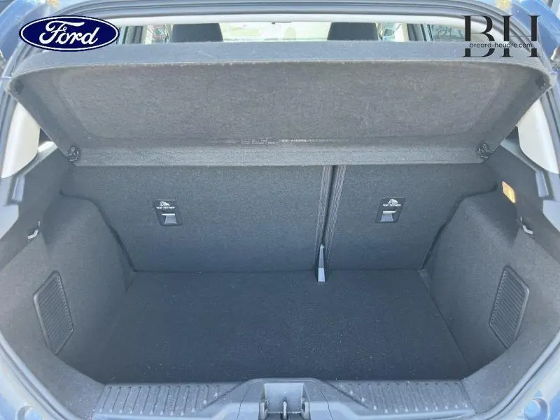 Coffre ouvert vu de l'arrière d'une Ford Fiesta 2022, intérieur noir avec banquette rabattable et cache-bagages.
