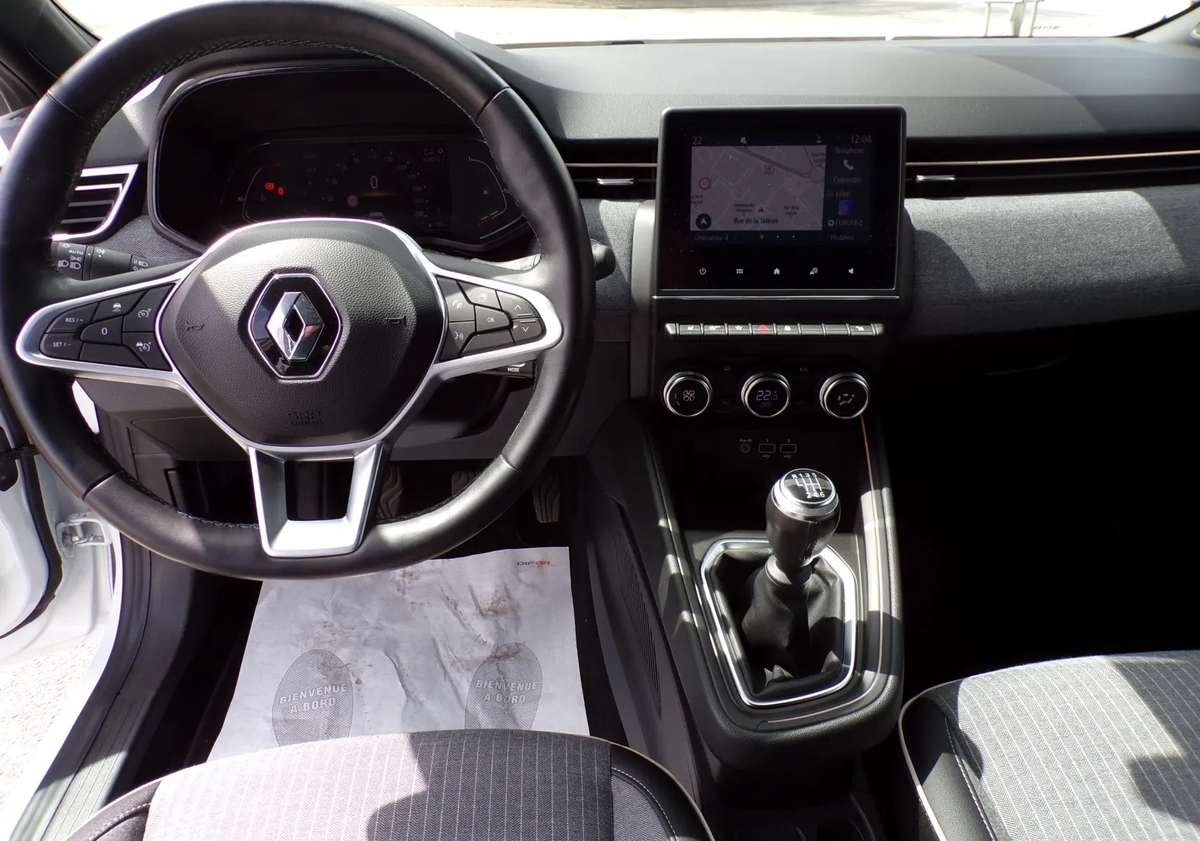 Intérieur de la Renault Clio V blanche 2022, vue frontale sur le volant multifonction et la console avec boîte manuelle.