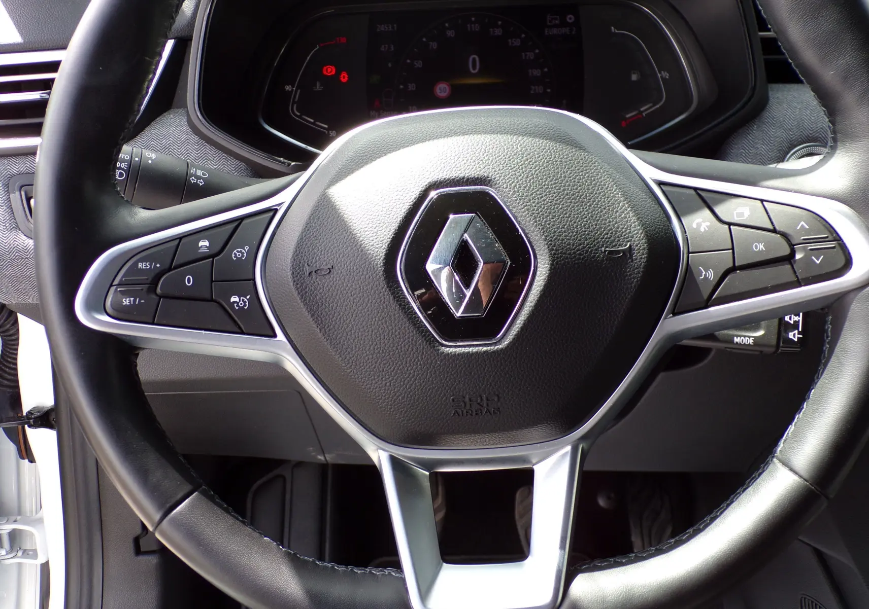 Gros plan sur le volant cuir noir de la Renault Clio V 1.3 TCE 140 ch blanc avec commandes multifonctions intégrées.