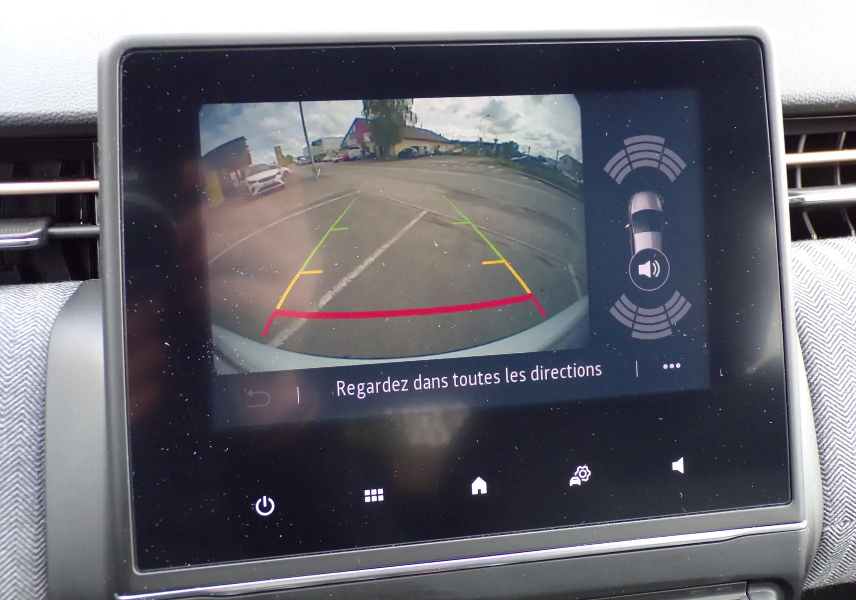 Écran central montrant la caméra de recul avec lignes de guidage et alertes de proximité sur Renault Clio V blanche.