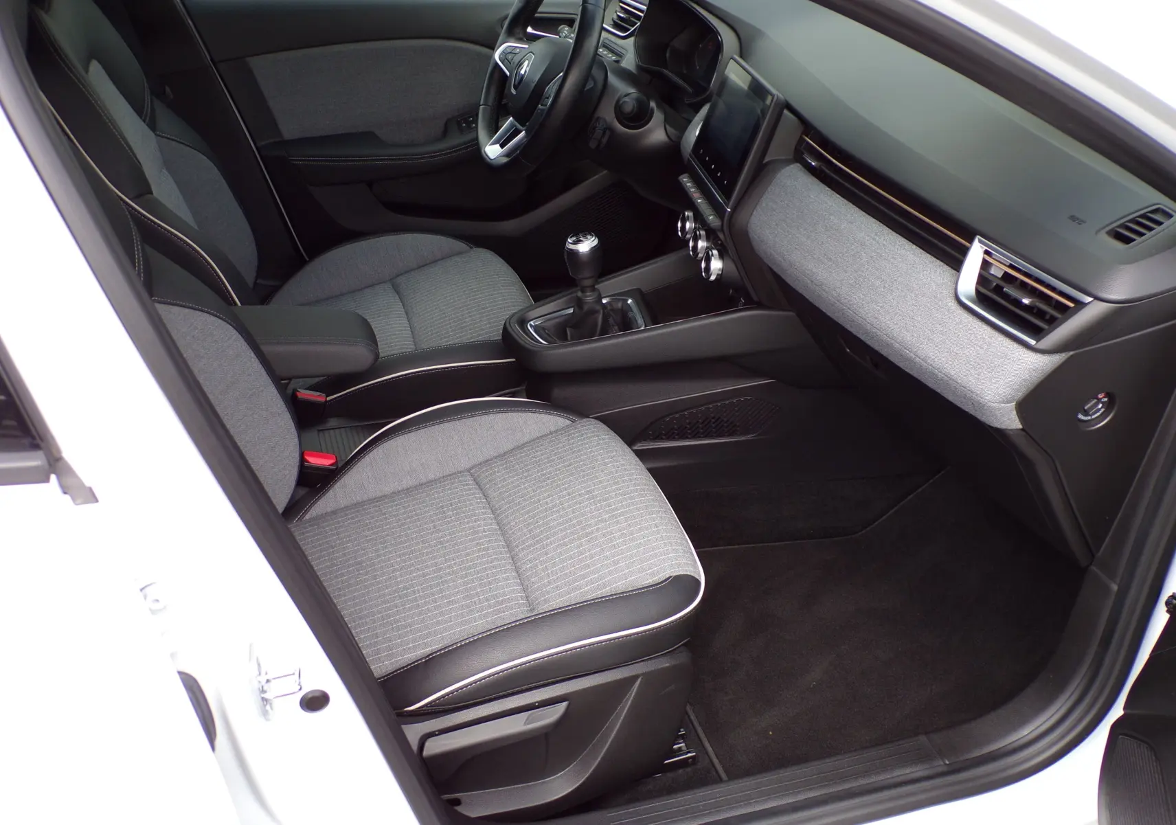 Vue intérieure côté conducteur de la Renault Clio V blanche 2022, sièges gris et tableau de bord moderne avec écran tactile.