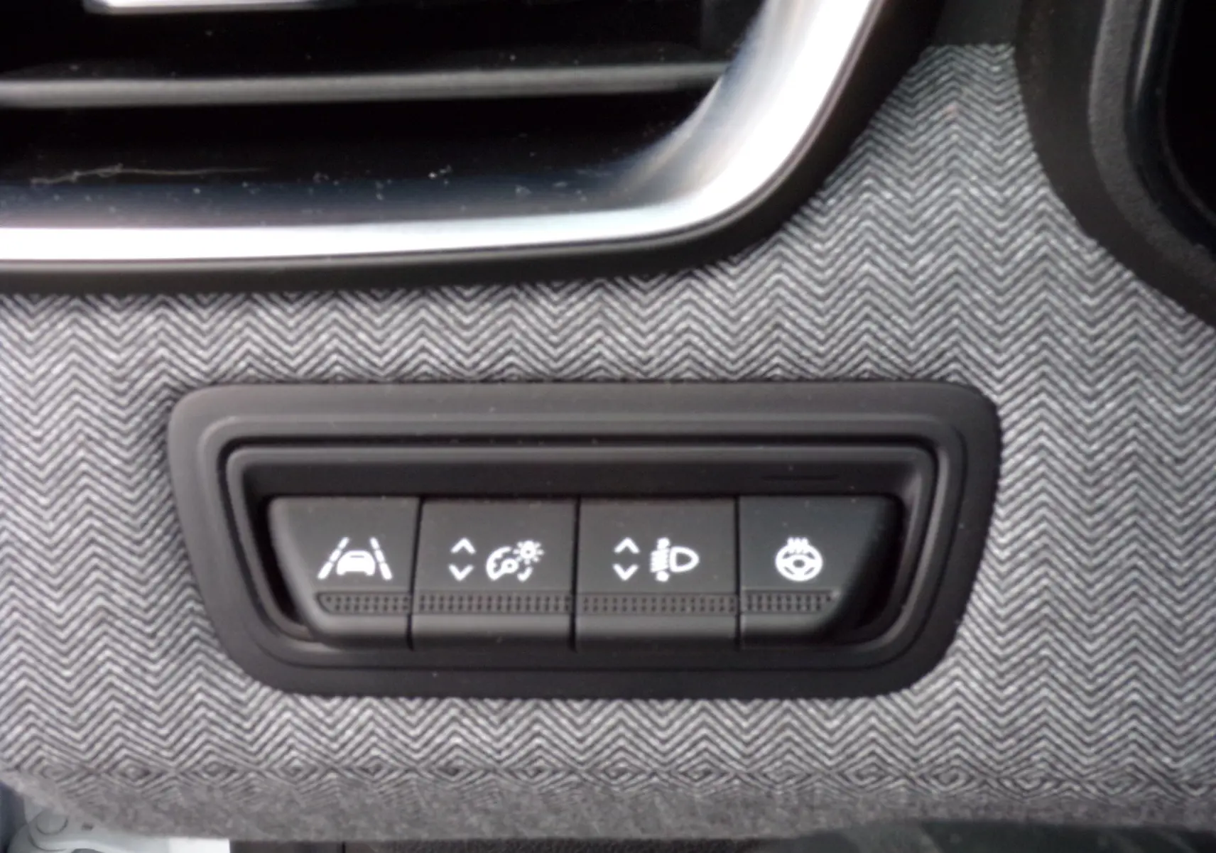 Gros plan sur les boutons de réglage d'assistance et éclairage intégrés dans la planche de bord tissu gris de la Renault Clio V blanche.