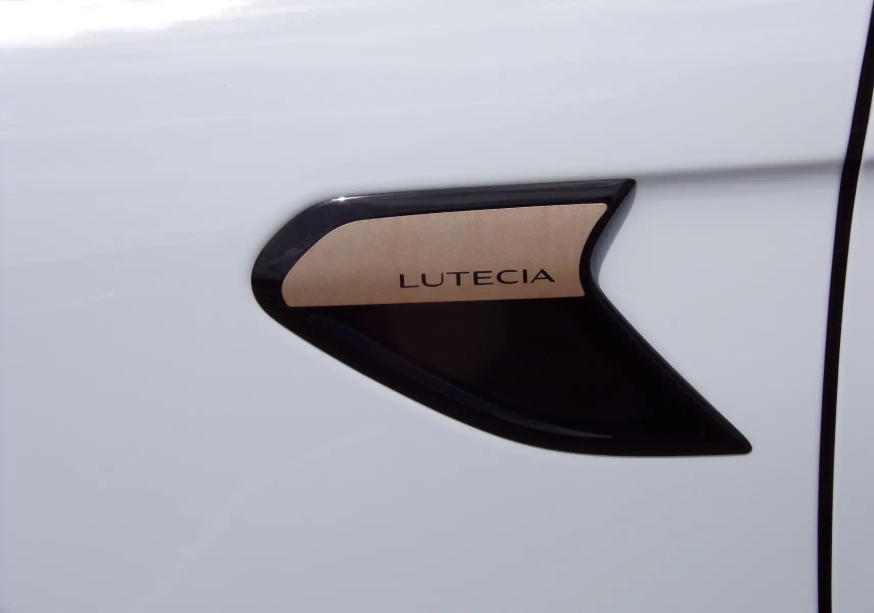 Détail de l'écusson LUTECIA noir et doré sur la porte blanche d'une Renault Clio V 2022.