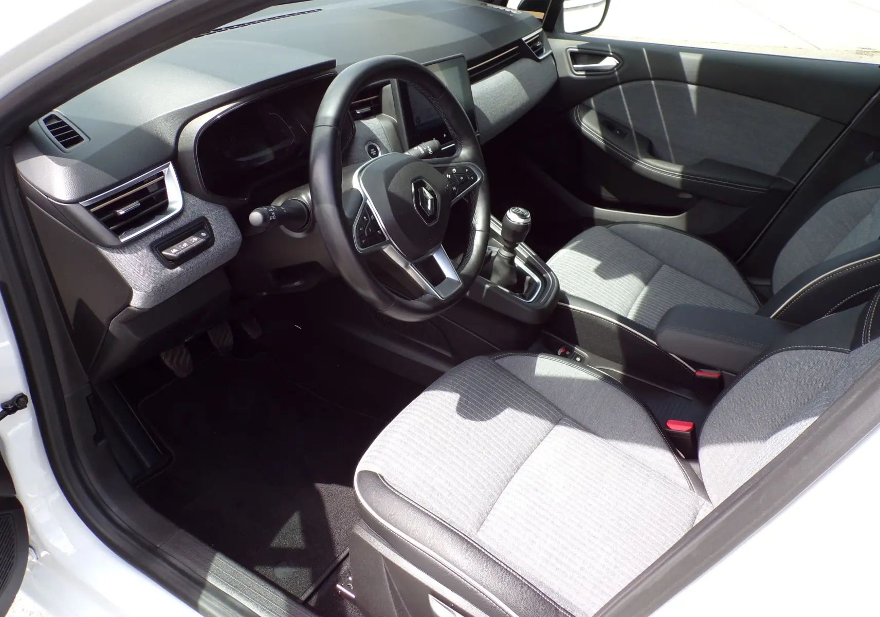 Intérieur avant droit de la Renault Clio V blanche 2022, volant multifonction et sellerie tissu gris clair.