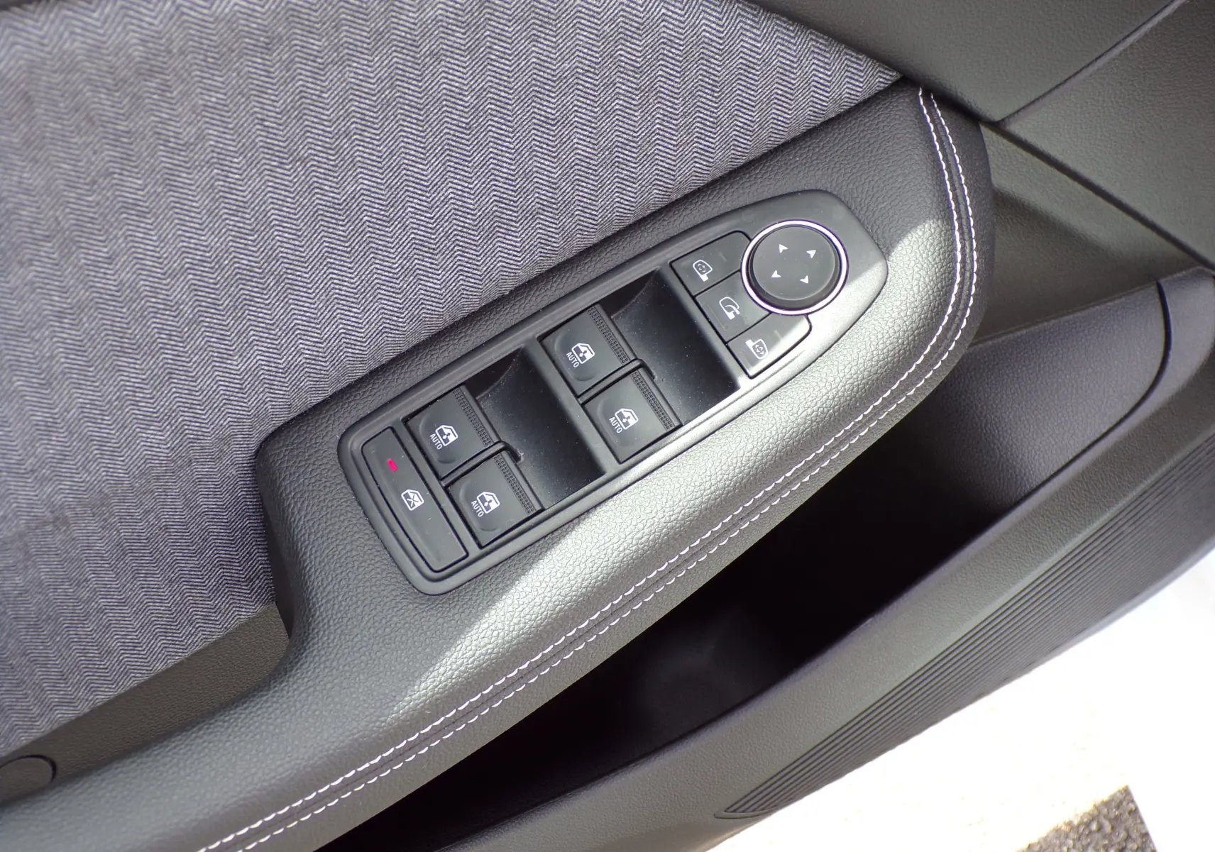 Gros plan sur les commandes de lève-vitres et réglage des rétroviseurs sur la porte côté gauche d'une Renault Clio V blanche.