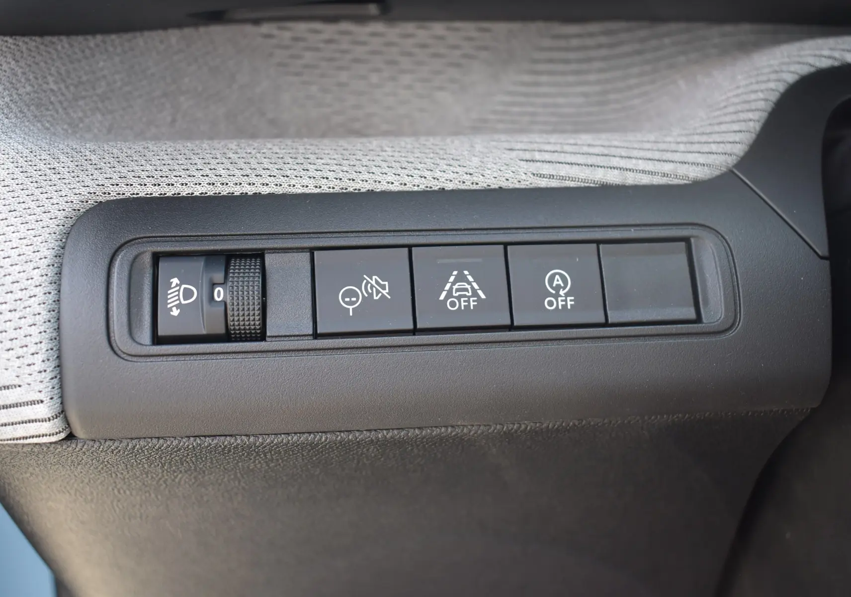 Gros plan sur les commandes de réglage des phares et aides à la conduite côté gauche intérieur d'une Citroën C3 bleu toit noir 2025.