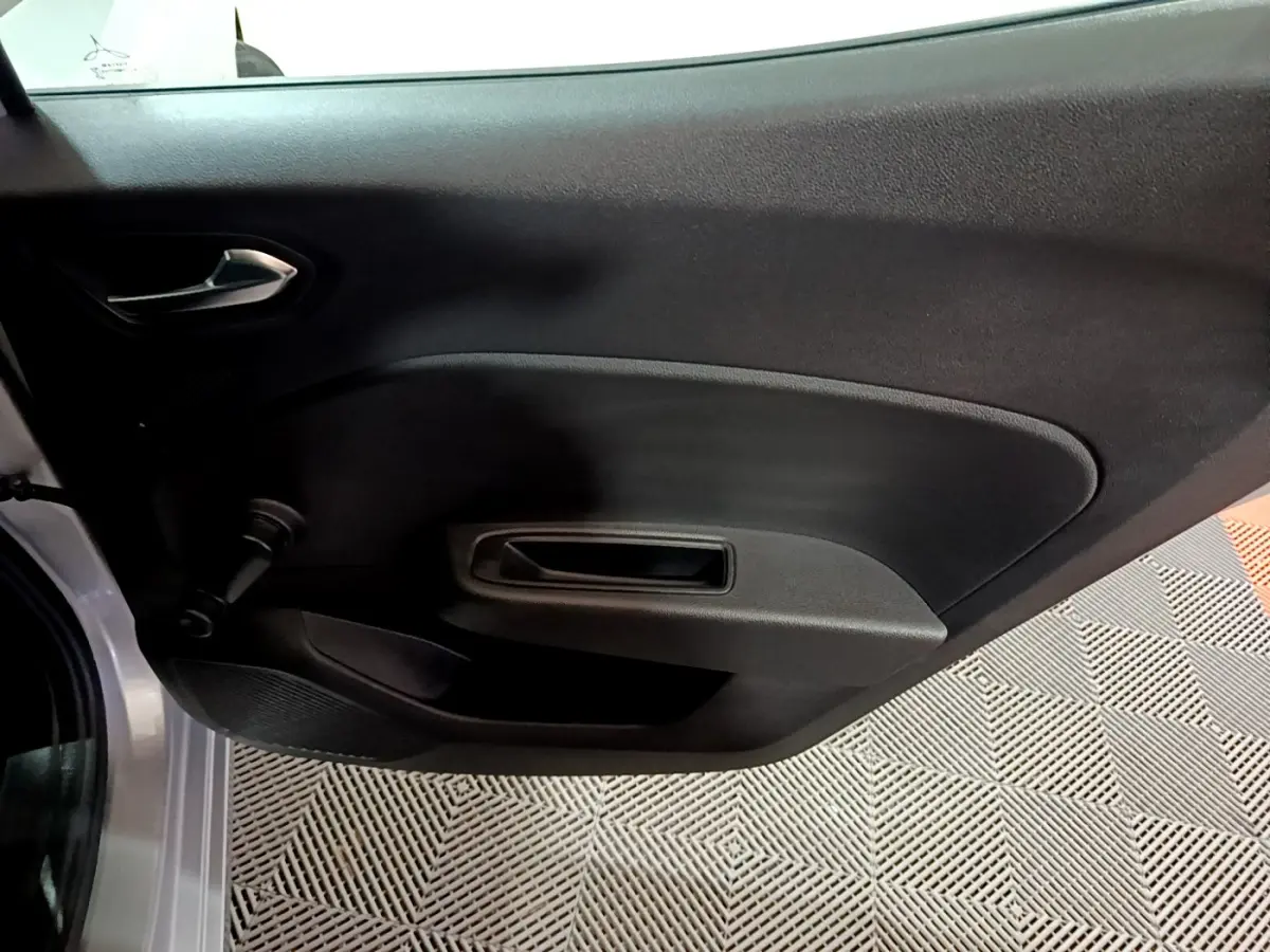 Vue rapprochée de la porte intérieure côté gauche d’une Renault Clio gris clair 2023 avec poignée noire et manivelle de vitre.