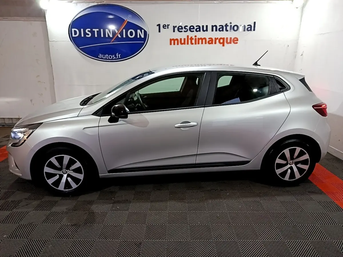 Profil droit d'une Renault Clio Equilibre TCe 90 gris clair 2023, avec jantes stylisées et feux arrière allumés.