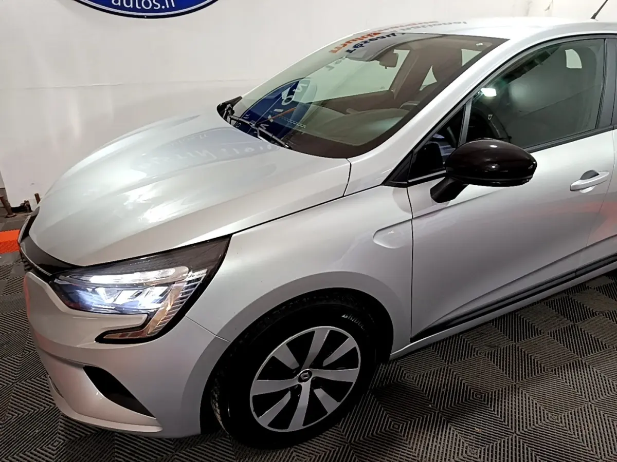 Vue 3/4 avant droit d'une Renault Clio gris clair 2023 avec phares LED allumés et rétroviseur noir brillant.