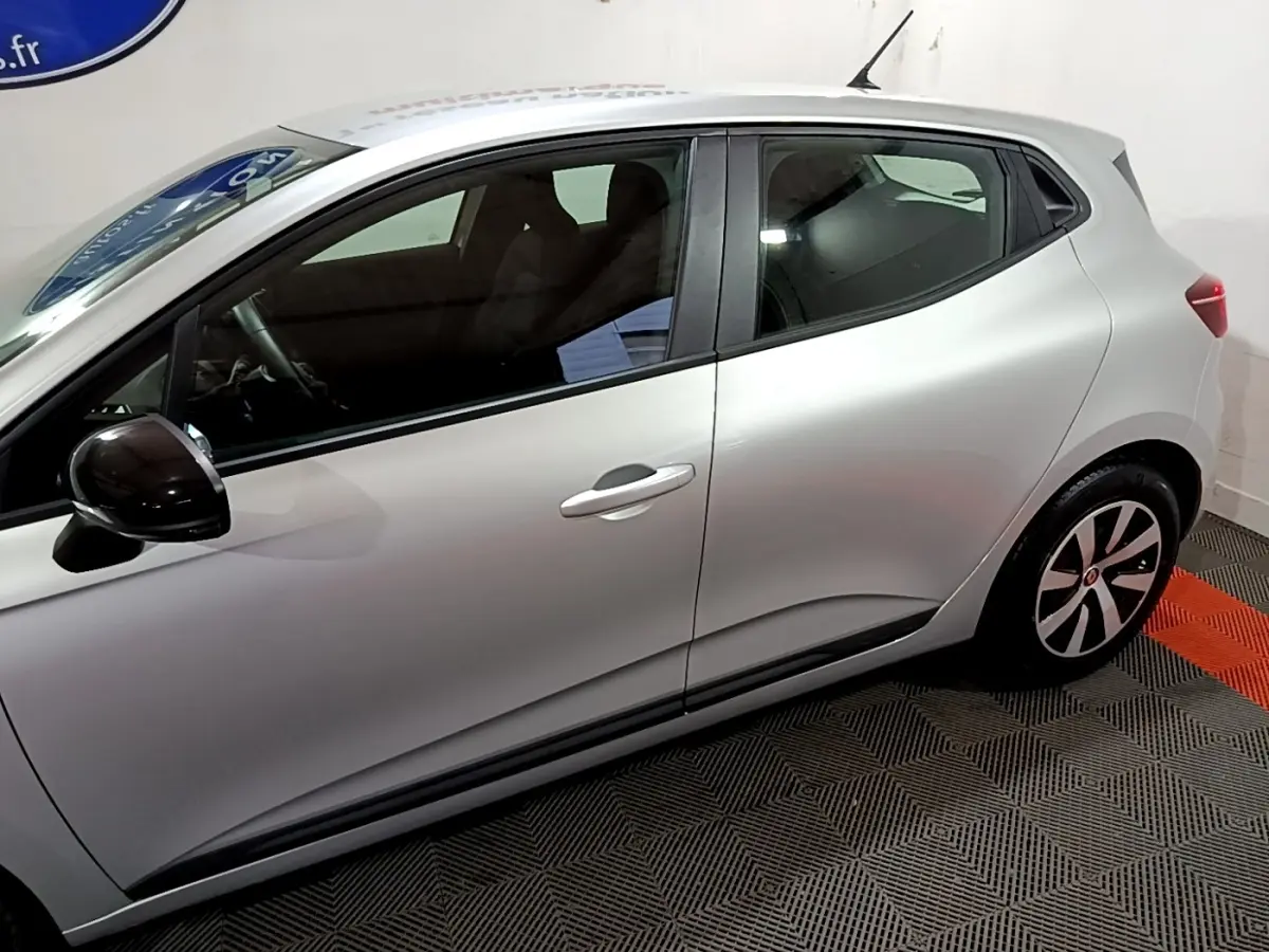 Profil côté gauche de la Renault Clio Equilibre TCe 90 gris clair, avec rétroviseur noir et jantes stylisées visibles.