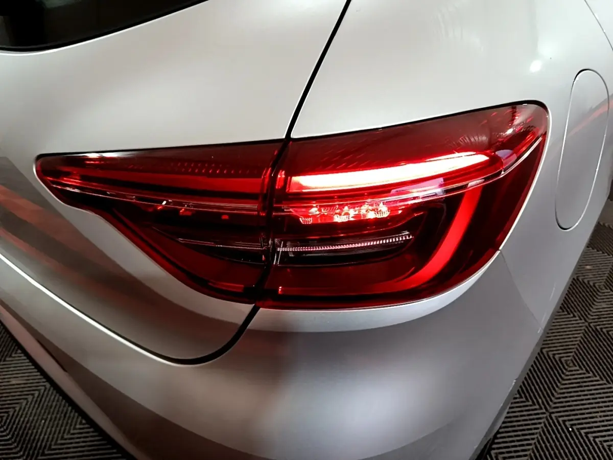 Gros plan sur le feu arrière droit rouge d'une Renault Clio gris clair, vue arrière côté droit.