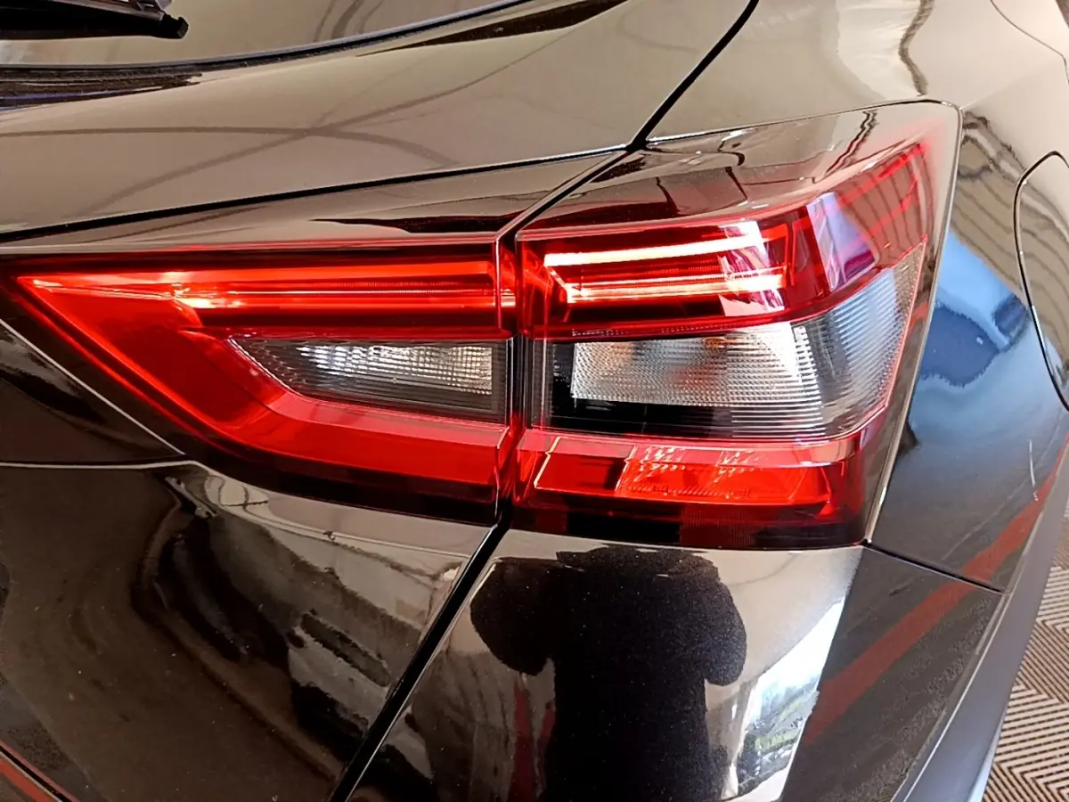 Gros plan sur le feu arrière droit rouge et blanc d’un Nissan Juke noir brillant, reflet de l’environnement visible.