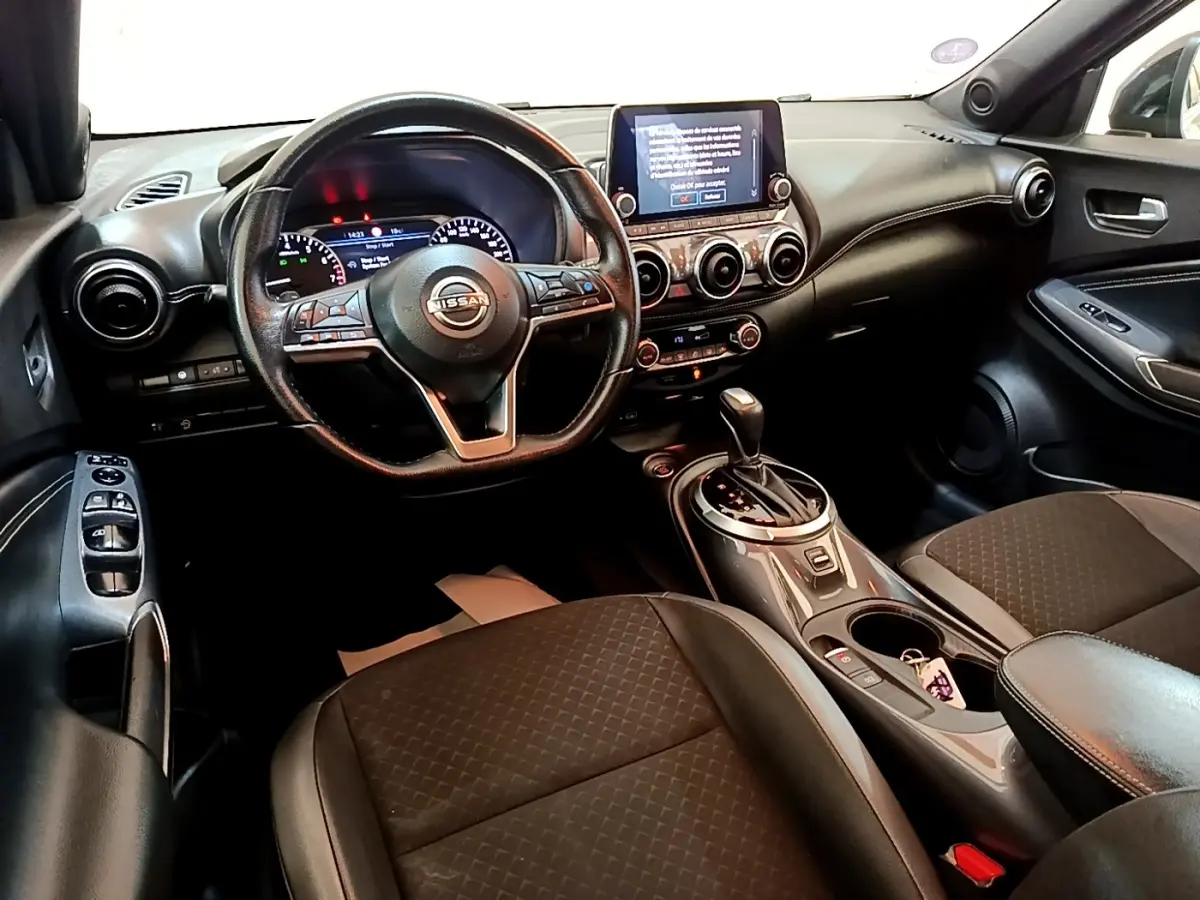 Vue intérieure côté conducteur du tableau de bord et console centrale du Nissan Juke noir avec écran tactile et volant multifonctions.