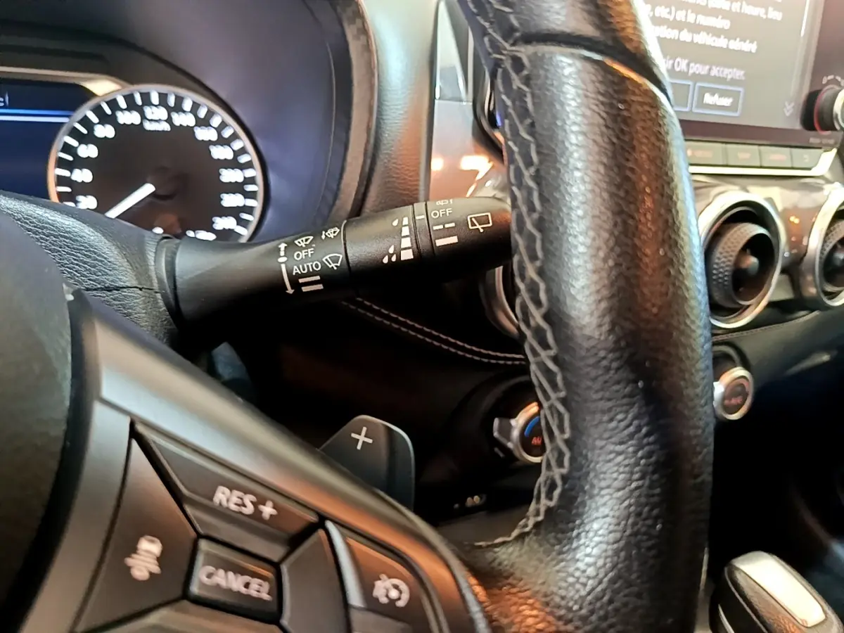 Vue rapprochée du volant noir du Nissan Juke 2022, montrant les commandes multifonctions et le tableau de bord lumineux.
