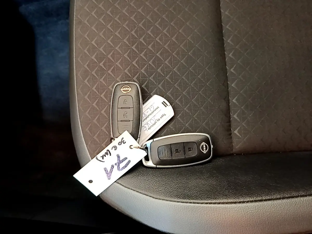 Gros plan sur deux clés Nissan posées sur un siège tissu noir à motifs géométriques à l'intérieur du véhicule.