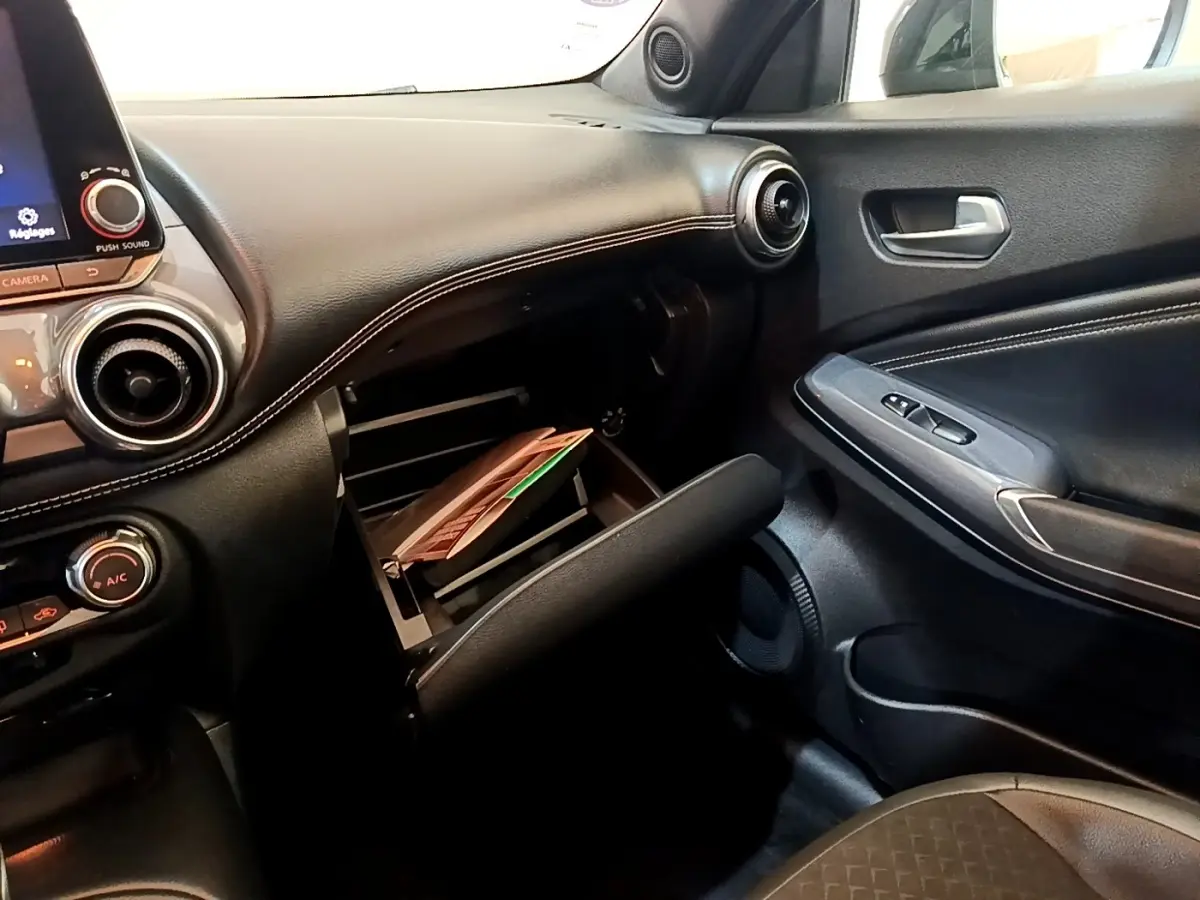 Vue intérieure côté passager du tableau de bord noir du Nissan Juke 2022 avec boîte à gants ouverte et porte en similicuir.