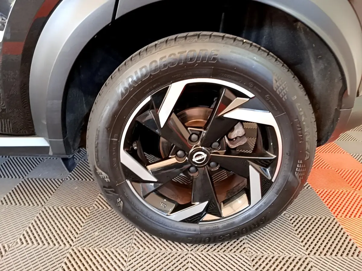 Gros plan sur la roue avant droite du Nissan Juke noir 2022 avec jante alliage bicolore et pneu Bridgestone.