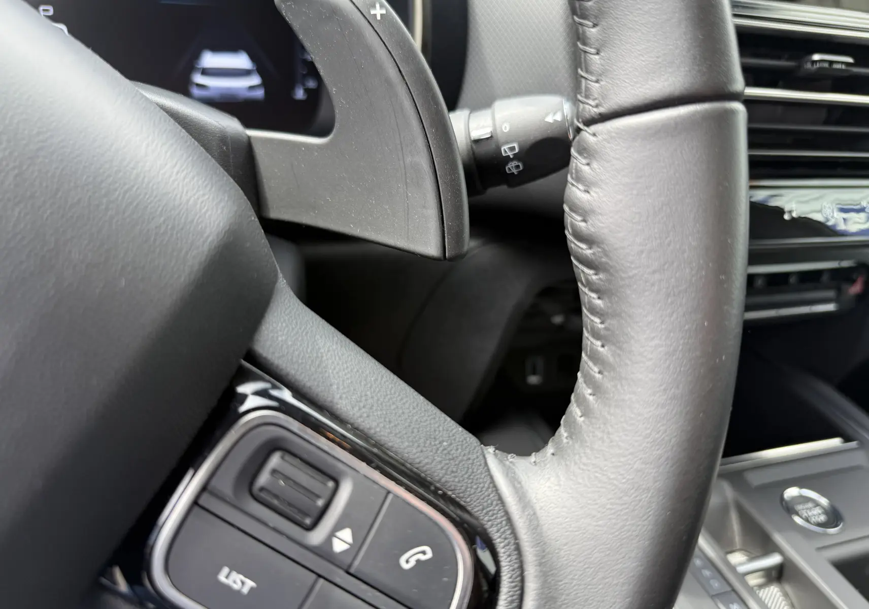 Gros plan sur le volant en cuir noir du Citroën C5 Aircross Hybrid 2025, avec commandes intégrées et palette de changement de vitesse.