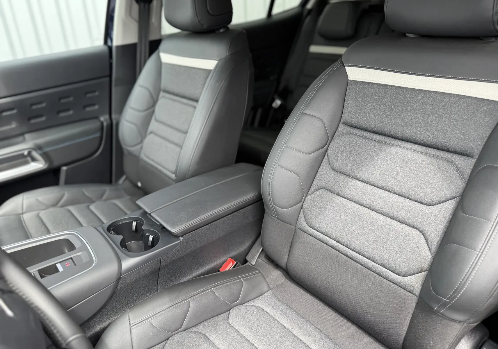 Vue intérieure rapprochée des sièges avant gris et noir du Citroën C5 Aircross Hybrid 145 e-DSC6 Max avec accoudoir central.
