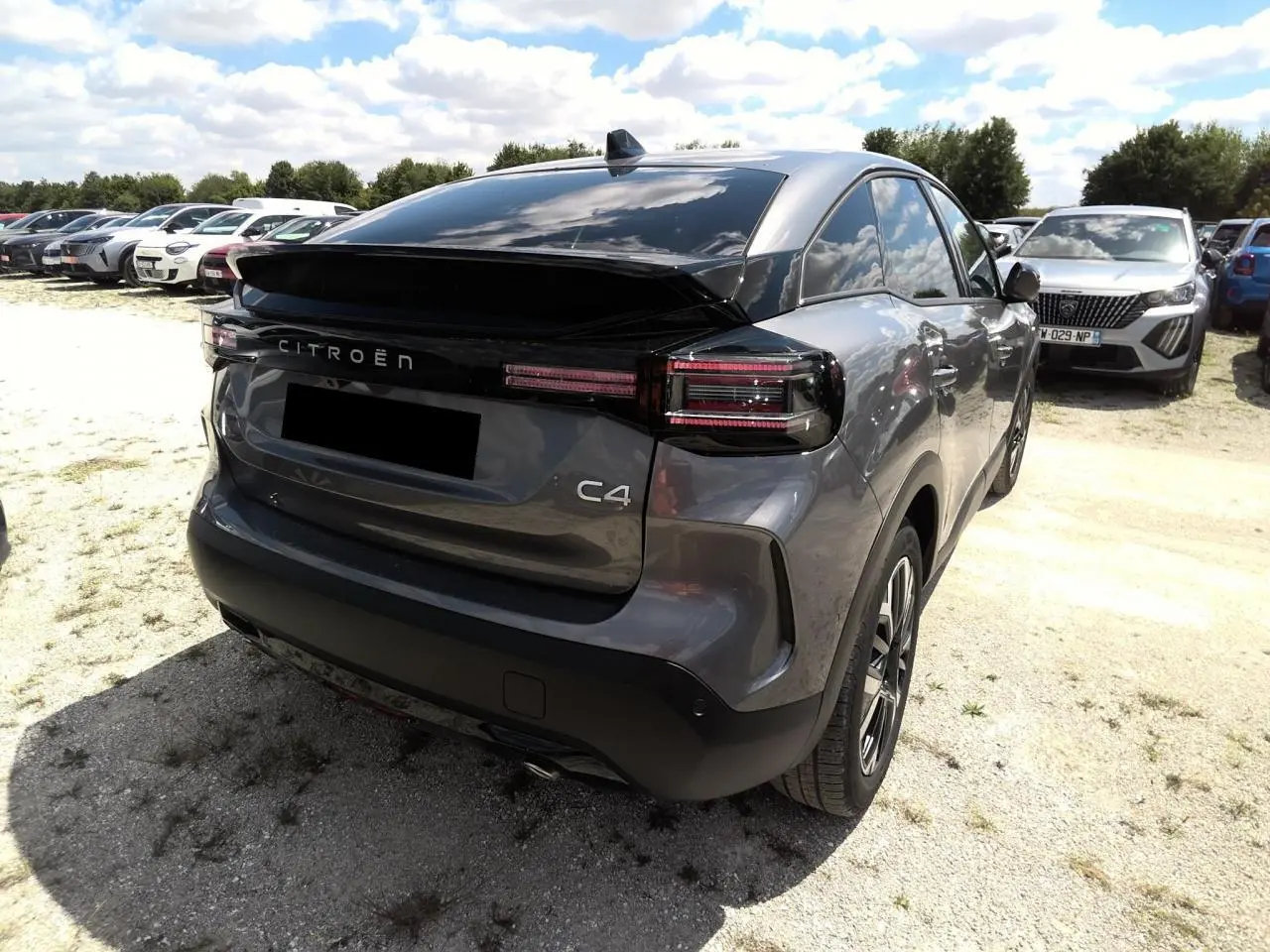 Vue 3/4 arrière droite d'une Citroën C4 Hybrid 145 gris Mercury avec feux arrière LED et toit noir brillant.