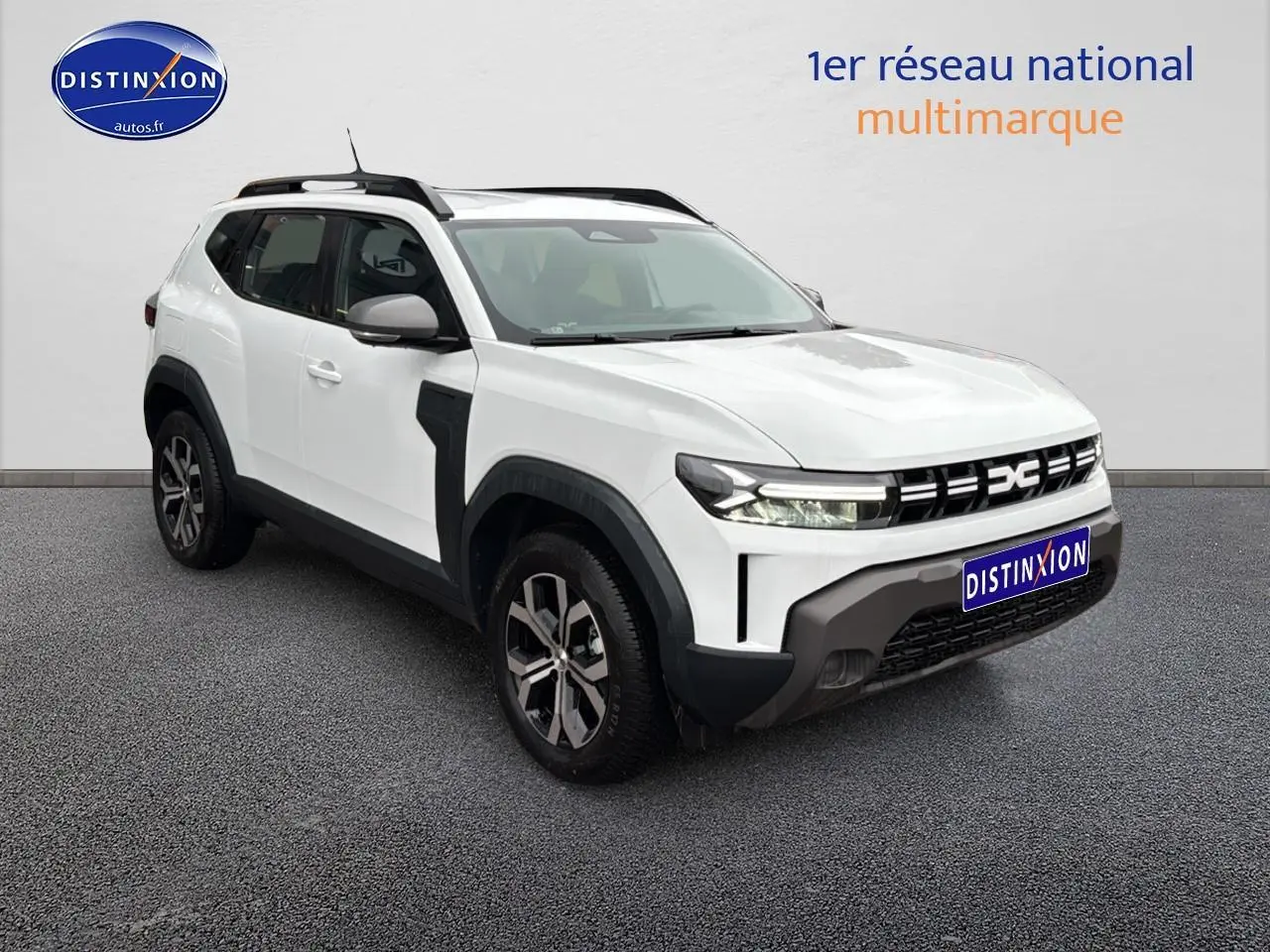 SUV Dacia Duster blanc arctic en 3/4 avant droit avec jantes alu et barres de toit noires visibles.