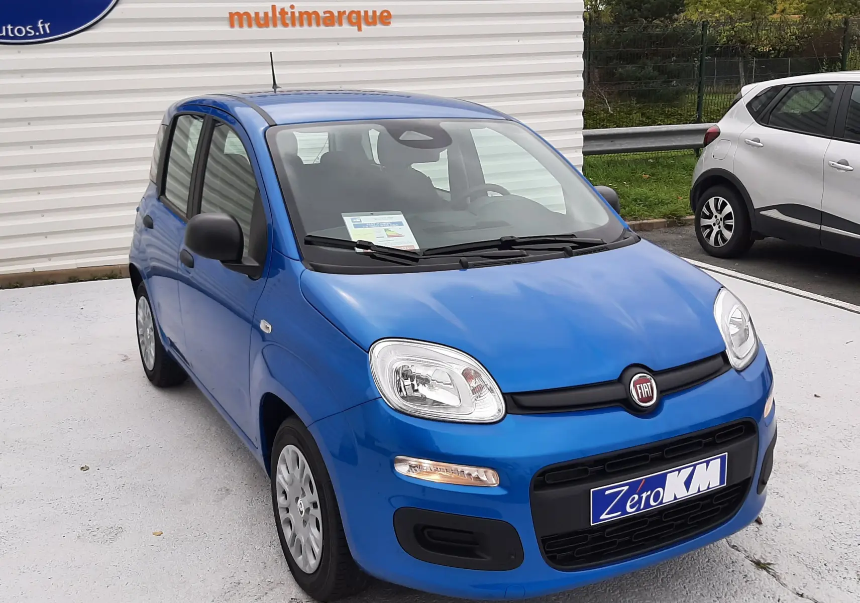 Vue 3/4 avant d'une Fiat Panda 2025 bleu Italia avec plaque Zero KM, garée devant un mur blanc.
