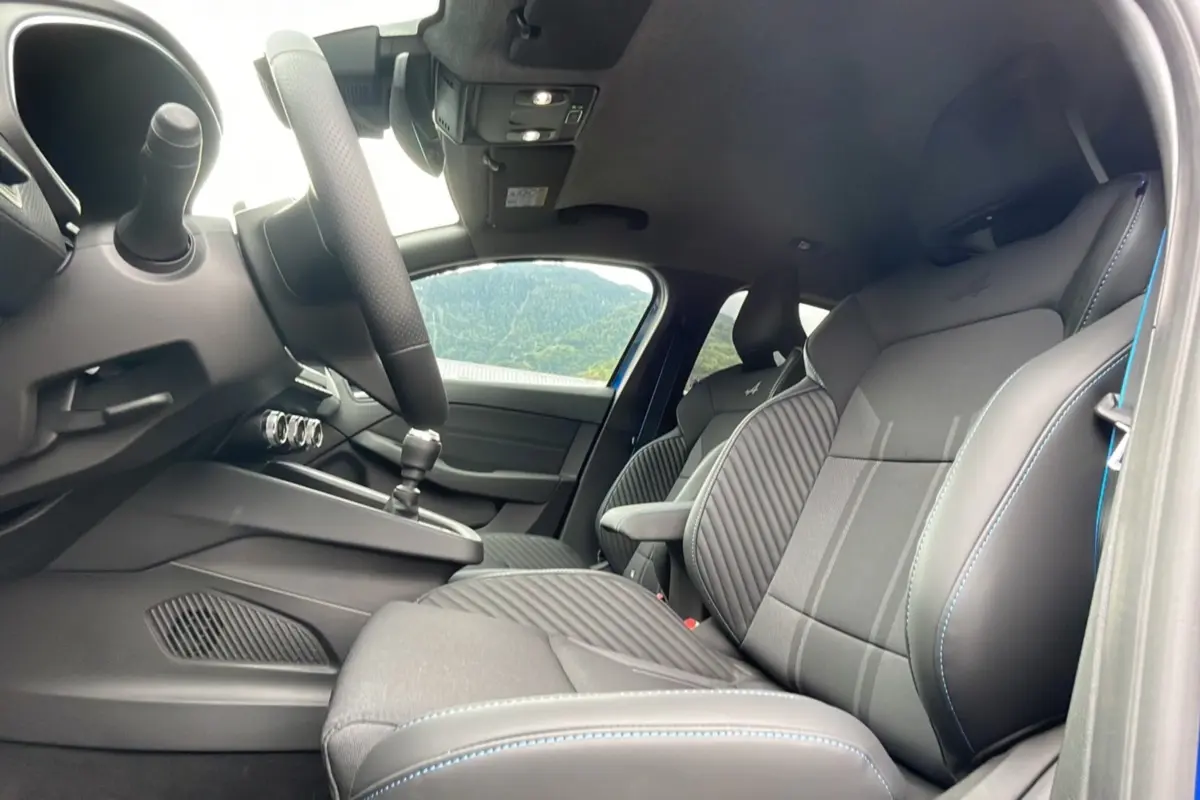 Intérieur avant de la Renault Clio V E-Tech 145 Esprit Alpine 2025, sièges noirs avec surpiqûres bleues et volant visible.