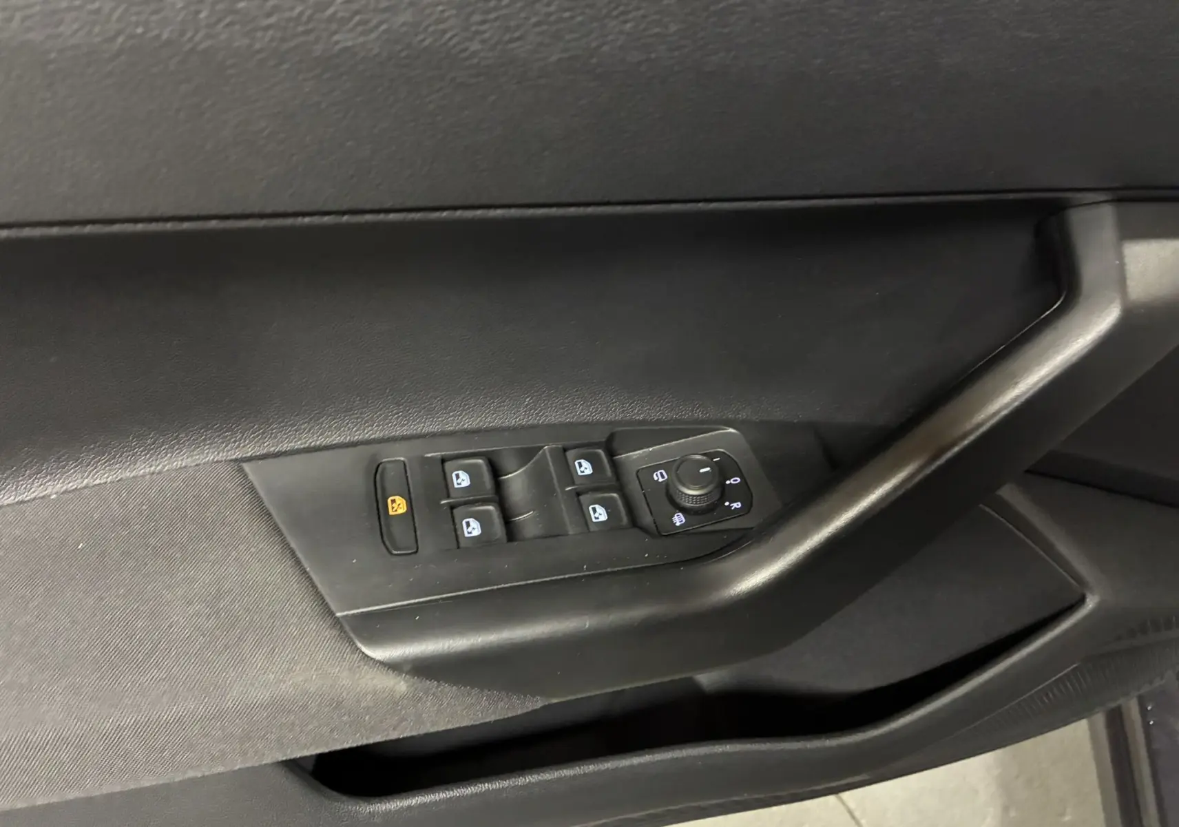 Gros plan sur la commande des vitres et réglages des rétroviseurs côté conducteur d'une Volkswagen Polo gris intérieur noir.