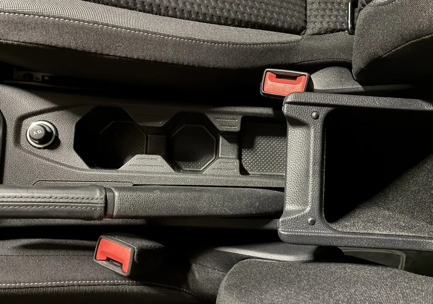 Gros plan sur la console centrale noire de la Volkswagen Polo gris, avec porte-gobelets et frein à main visible.