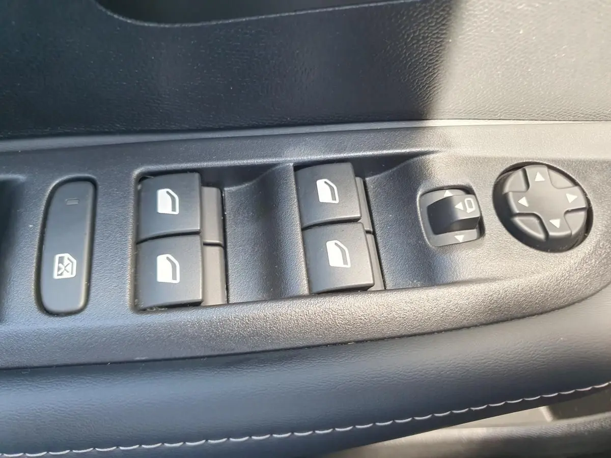 Gros plan sur les commandes de lève-vitres et réglage des rétroviseurs côté conducteur d'une Peugeot 208 1.2 Hybrid 110 gris Sellenium.