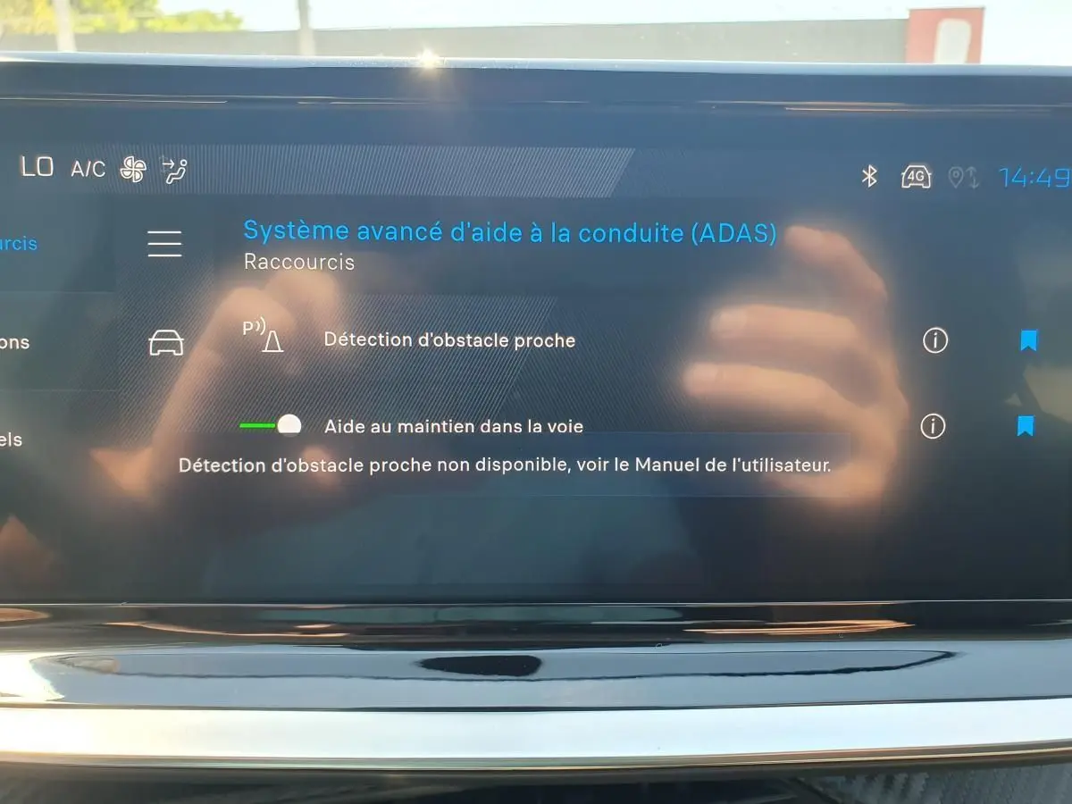 Écran tactile intérieur affichant le menu d’aide à la conduite du Peugeot 208 hybride, avec reflet des mains.