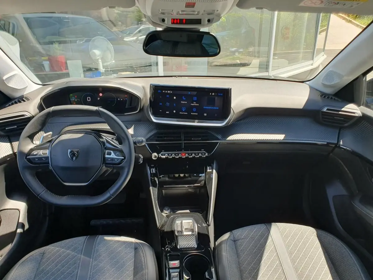 Vue intérieure avant de la Peugeot 208 1.2 Hybrid 110 Allure, tableau de bord noir avec écran tactile 10 pouces.
