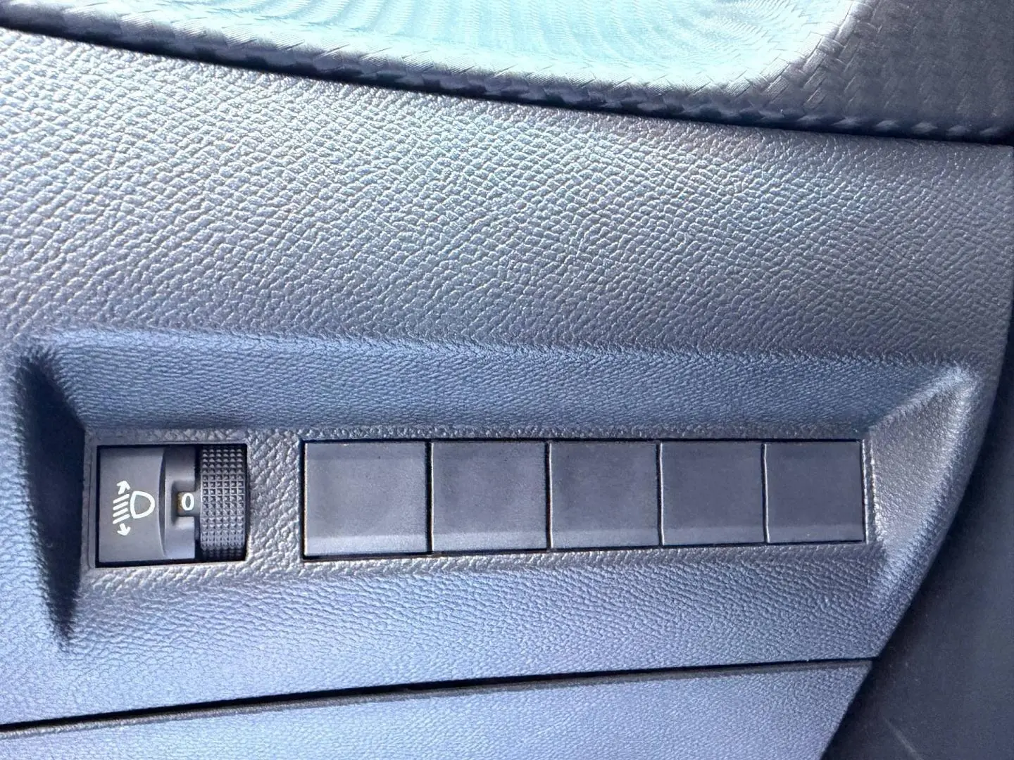 Gros plan sur le bouton de réglage des phares dans l’habitacle noir du Peugeot 208 jaune 2025.