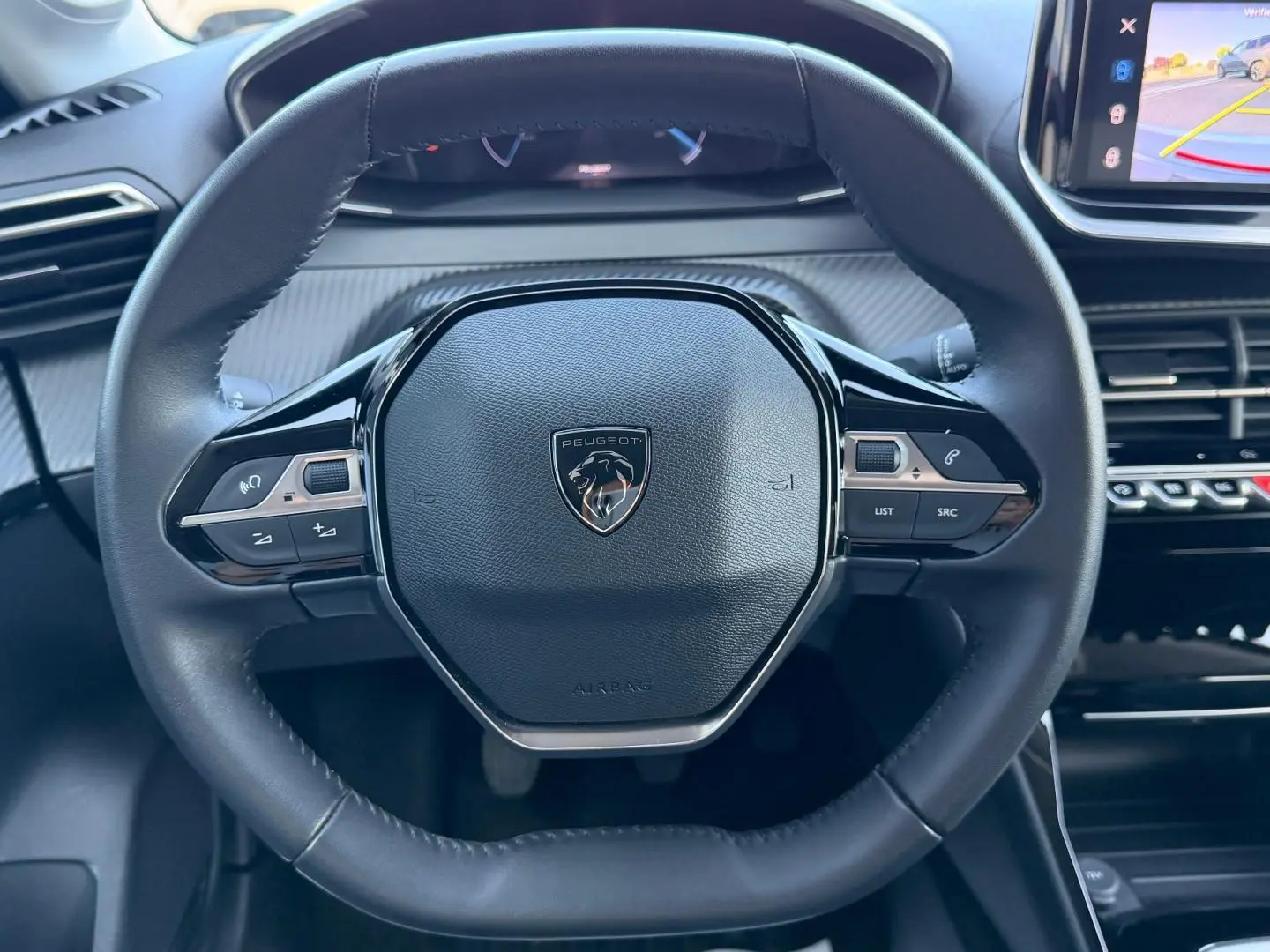Vue rapprochée du volant cuir noir de la Peugeot 208 2025 avec commandes intégrées et écran tactile visible à droite.