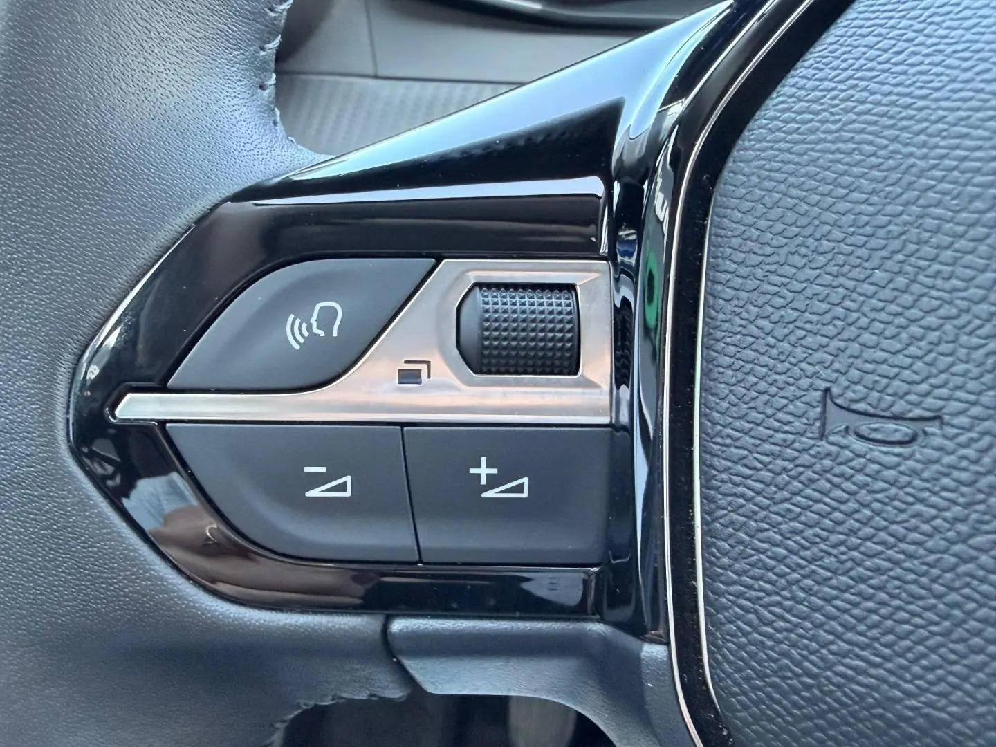 Gros plan sur les commandes audio noires et argentées situées sur le côté gauche du volant en cuir noir.
