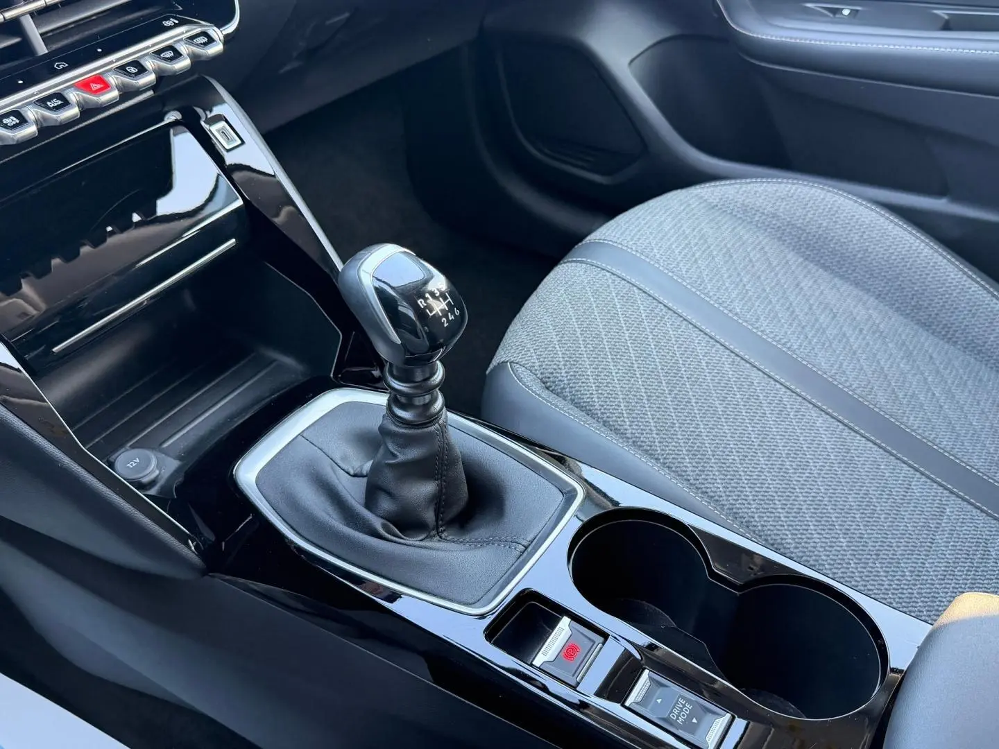 Vue rapprochée de la console centrale de la Peugeot 208 2025, avec levier de vitesse manuel et siège tissu gris.