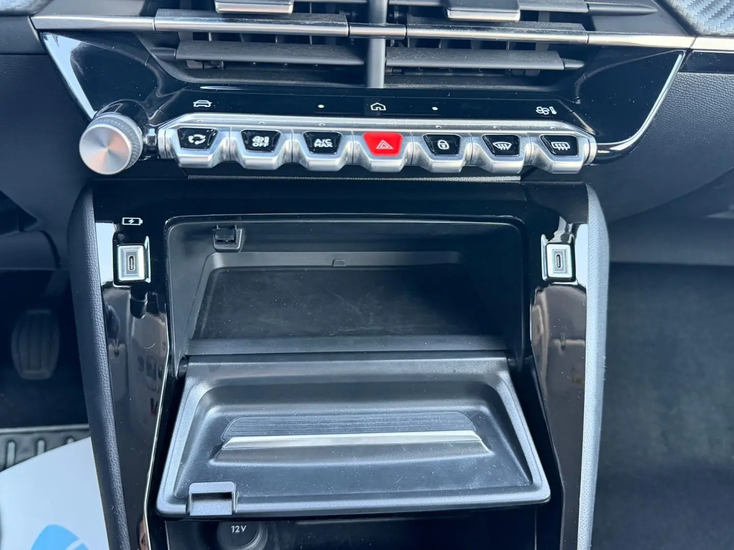 Vue rapprochée de la console centrale noire brillante de la Peugeot 208 1.2 100ch, avec commandes et rangement ouvert.