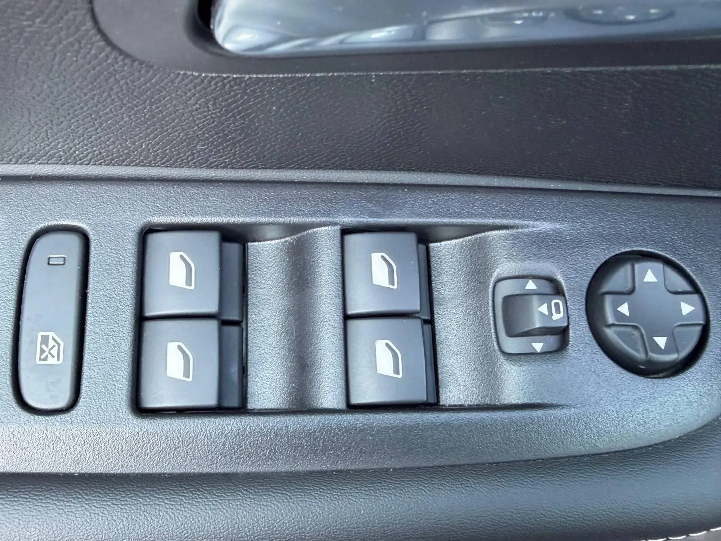 Gros plan sur les commandes électriques des vitres et des rétroviseurs côté conducteur d'une Peugeot 208 jaune 2025.